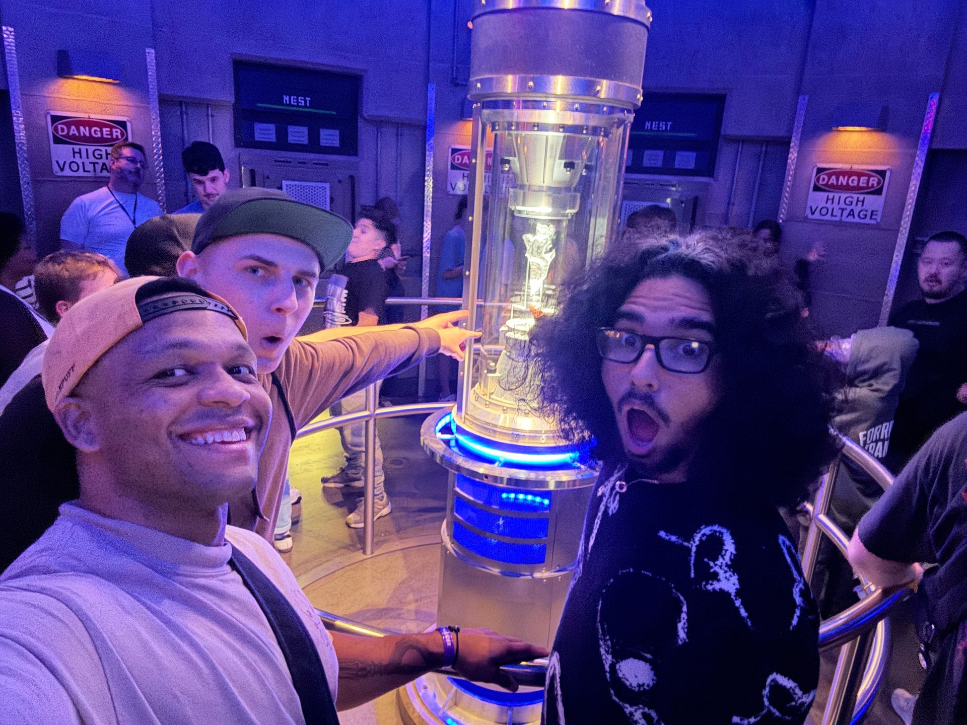 Three people posing indoors beside a glowing cylindrical exhibit at an arcade or museum.