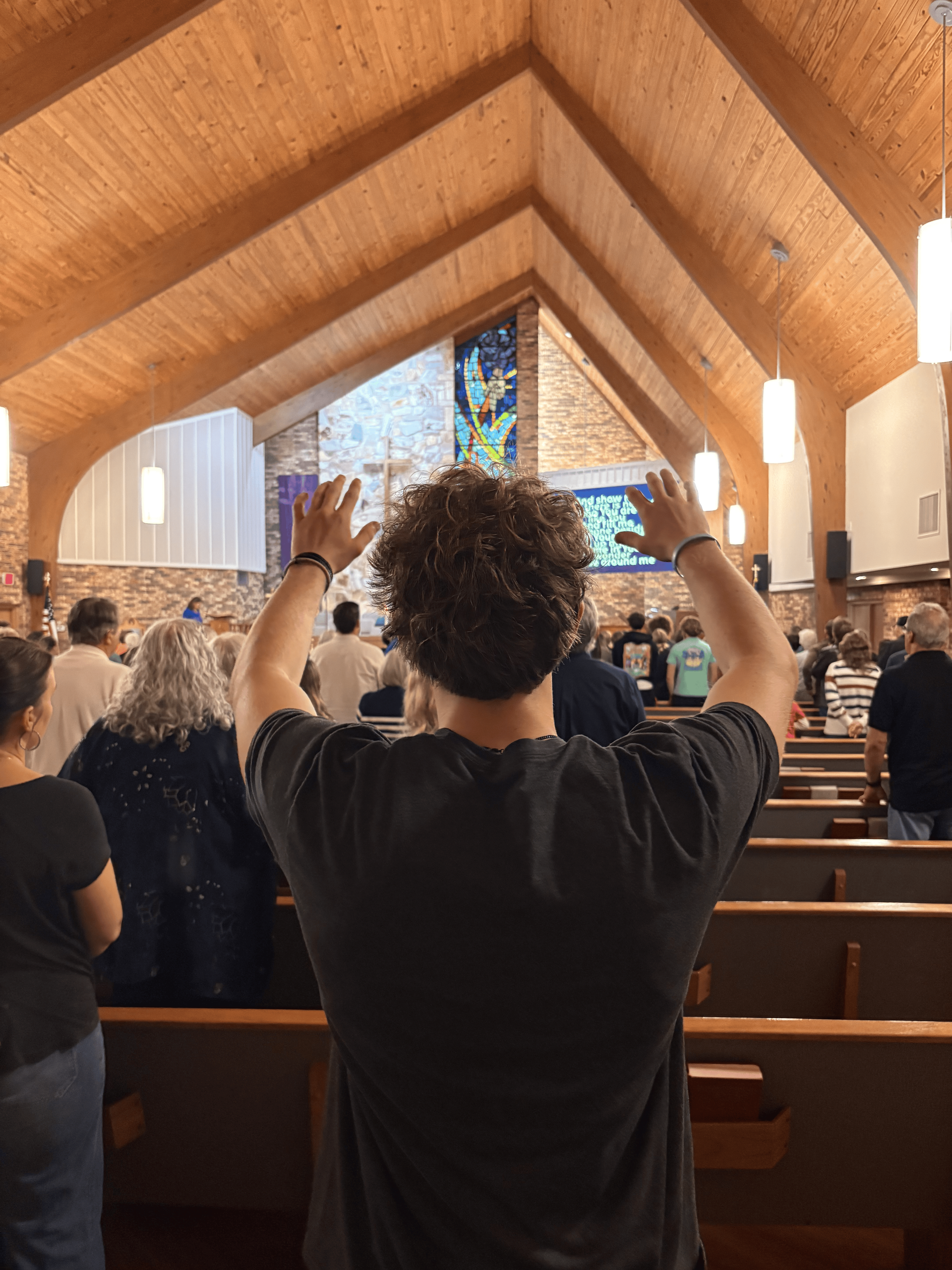 Congregants seated in a church pew with hands raised during a worship service