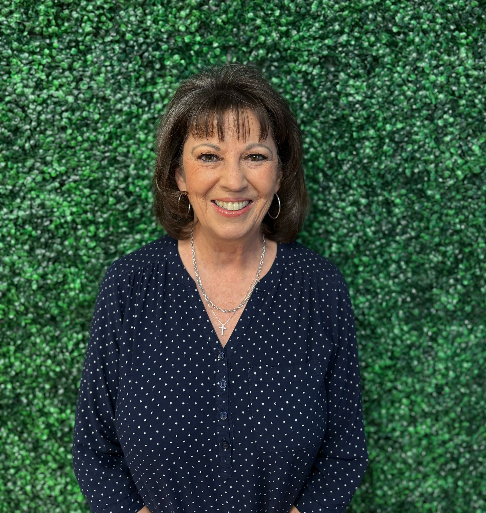 Woman smiling in a navy polka-dot blouse against a green leafy wall