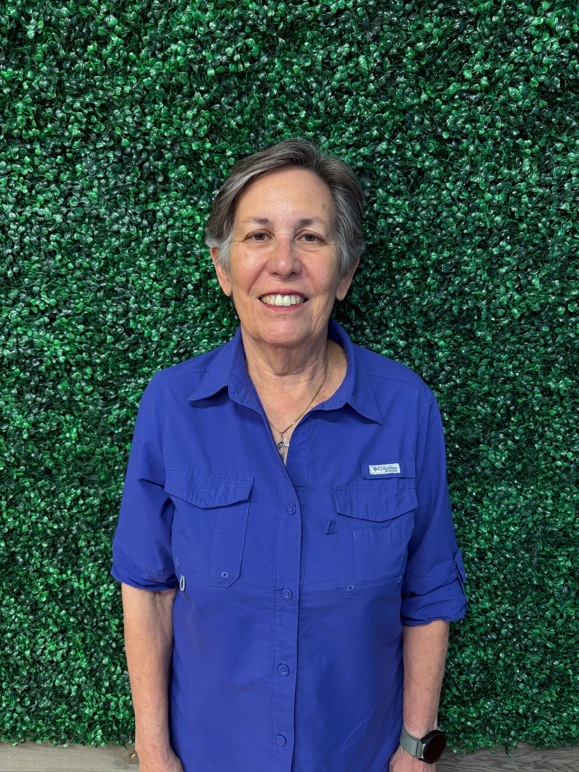 Person in a blue shirt standing in front of a green textured wall, smiling at the camera.