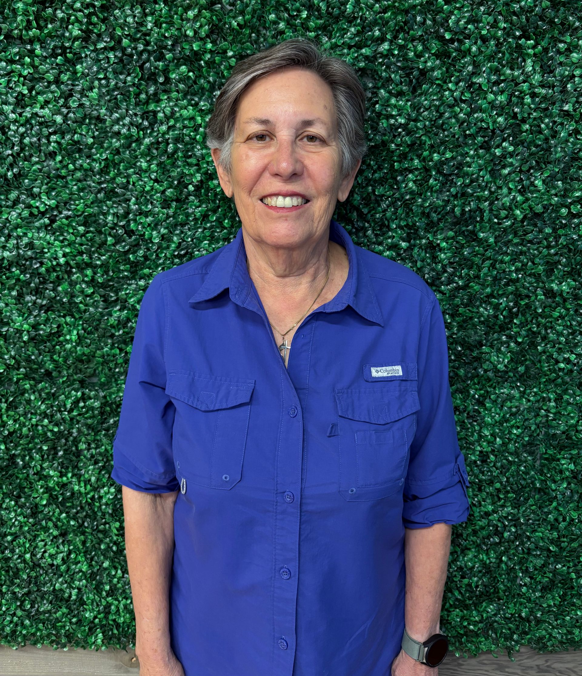 Smiling person in a blue shirt standing in front of a green textured backdrop