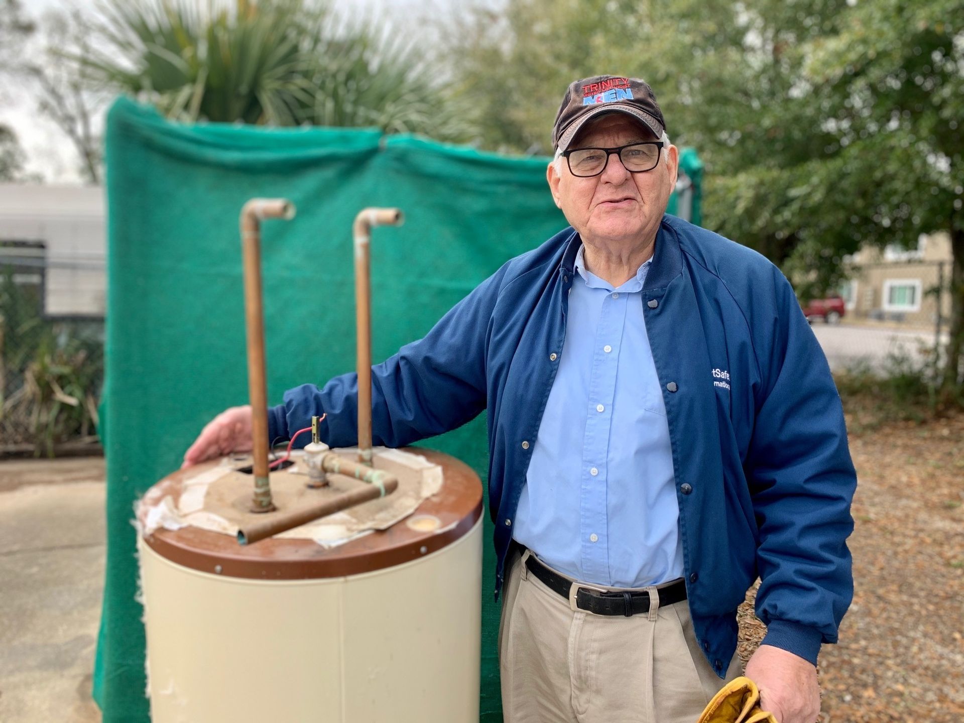 Man standing beside a beige utility pedestal with pipes, outdoors in front of a green tarp backdrop.
