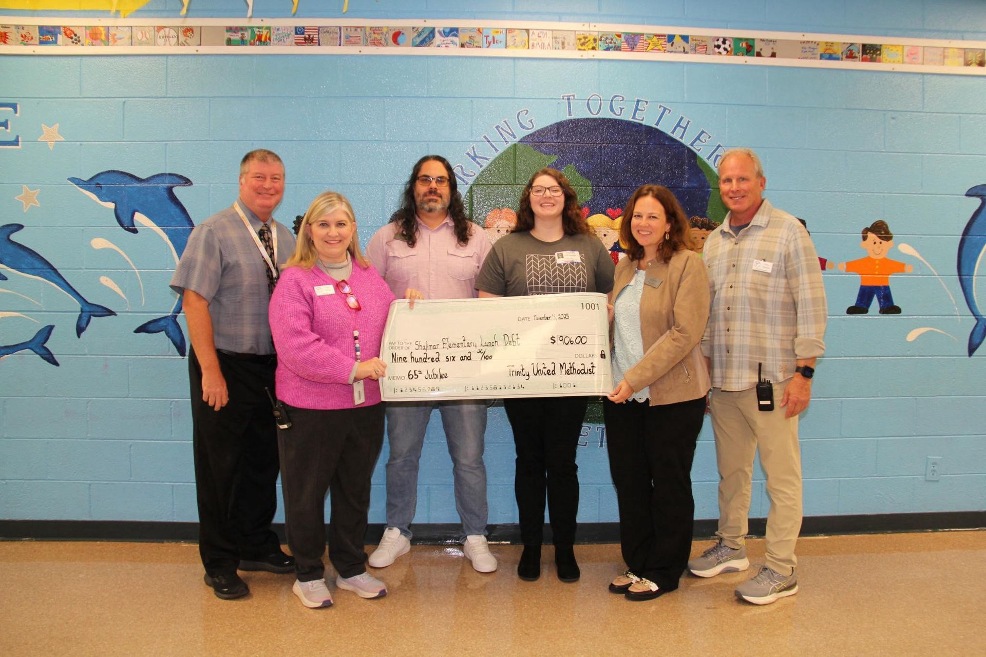 Six people holding a large check in front of a colorful mural with dolphins and fish