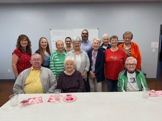 Group of people posing in a room behind a table with pink treats and drinks