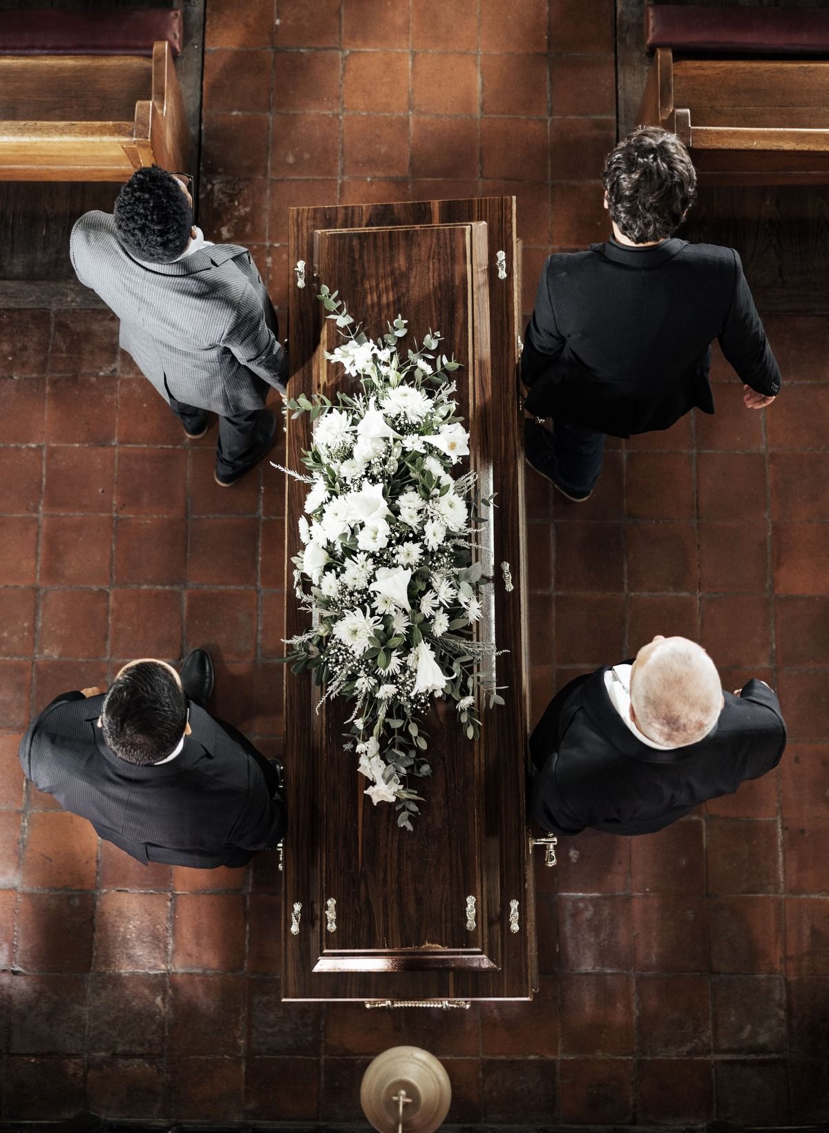 Mourners in black carry a flower-covered coffin at an outdoor funeral procession