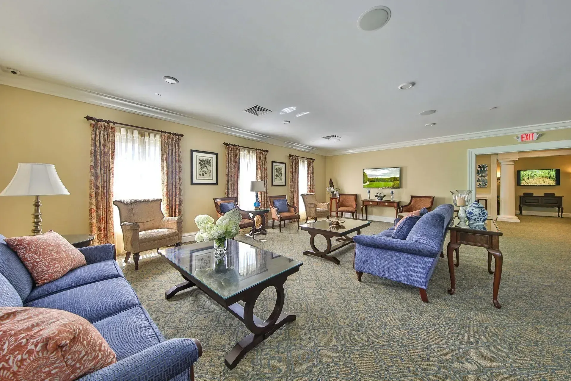 Bright living room with blue sofas, glass coffee table, dining area, and fireplace near a large window.