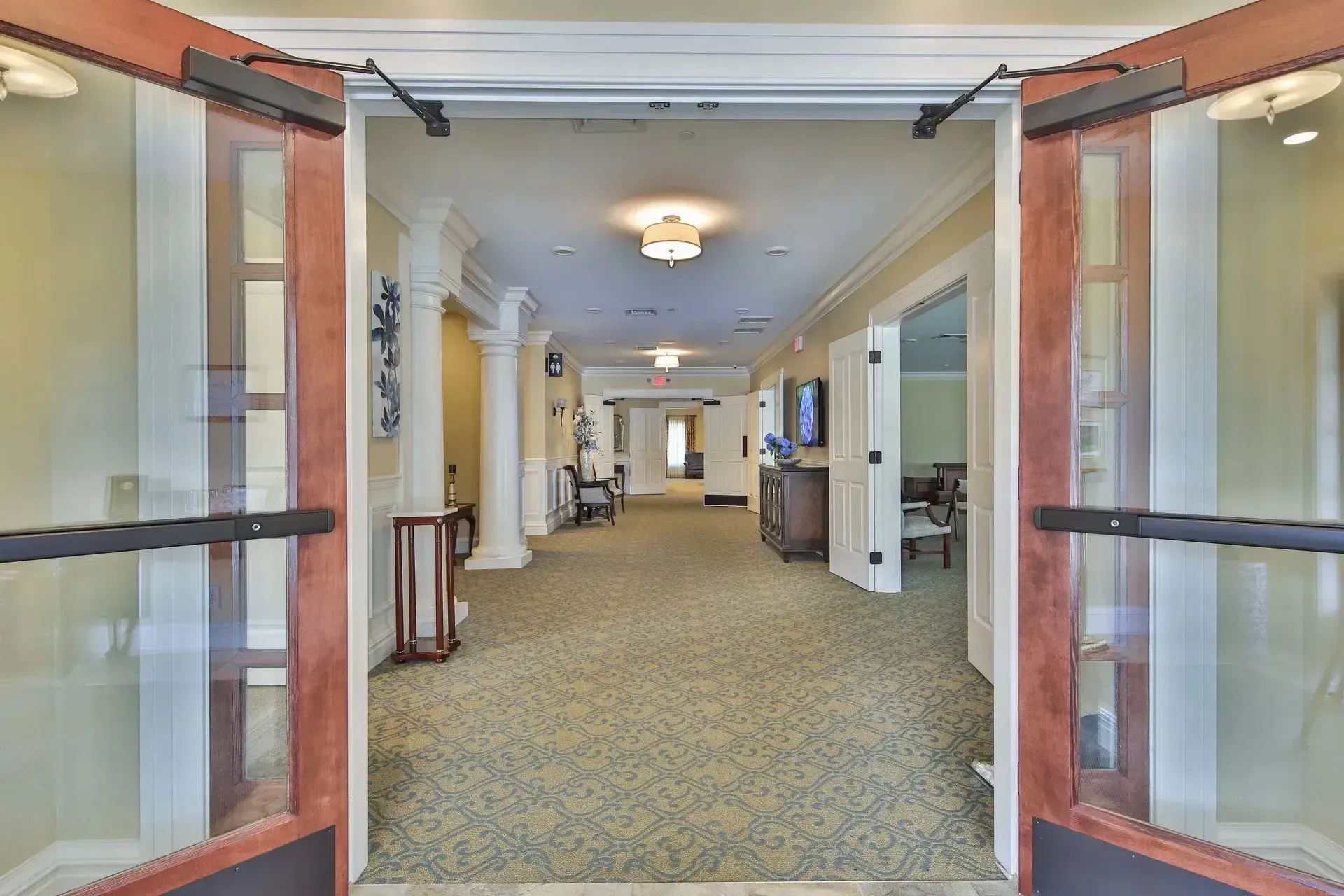 Open glass doors leading into a bright carpeted hallway with columns and ceiling lights