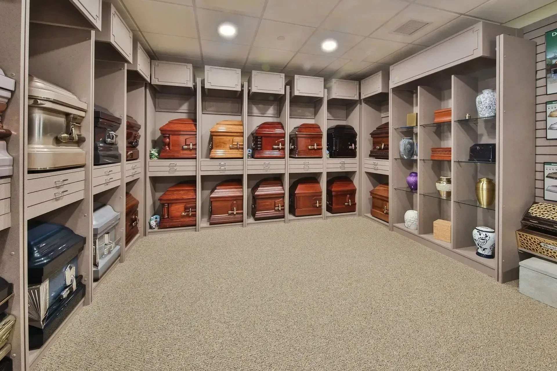 Organized storage room with shelves of folded blankets, orange bags, and decorative items beneath recessed lighting