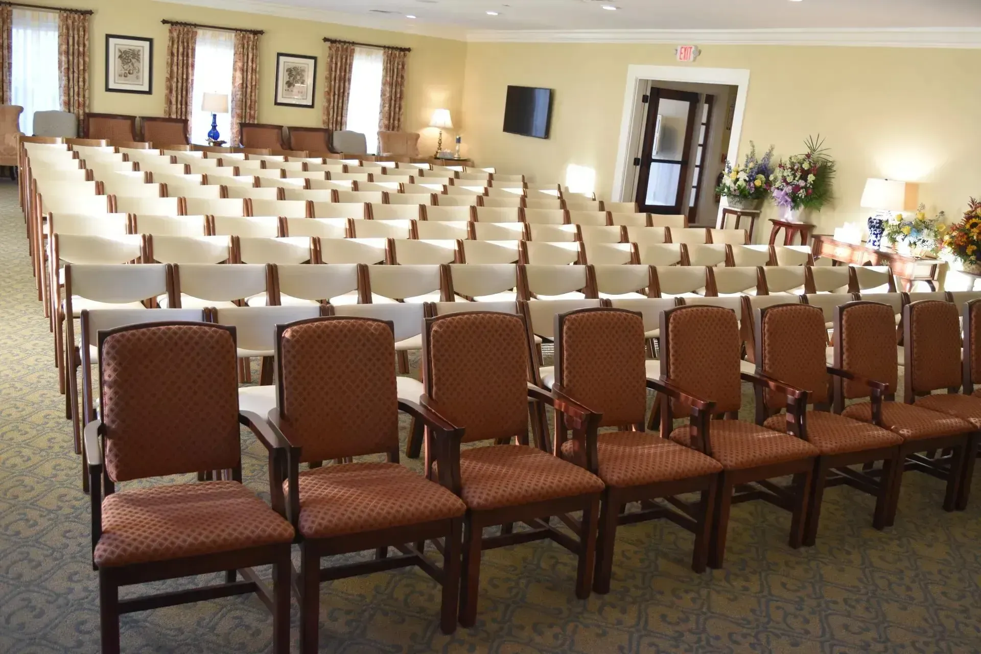 Empty banquet hall with rows of brown chairs facing a front doorway and framed wall art
