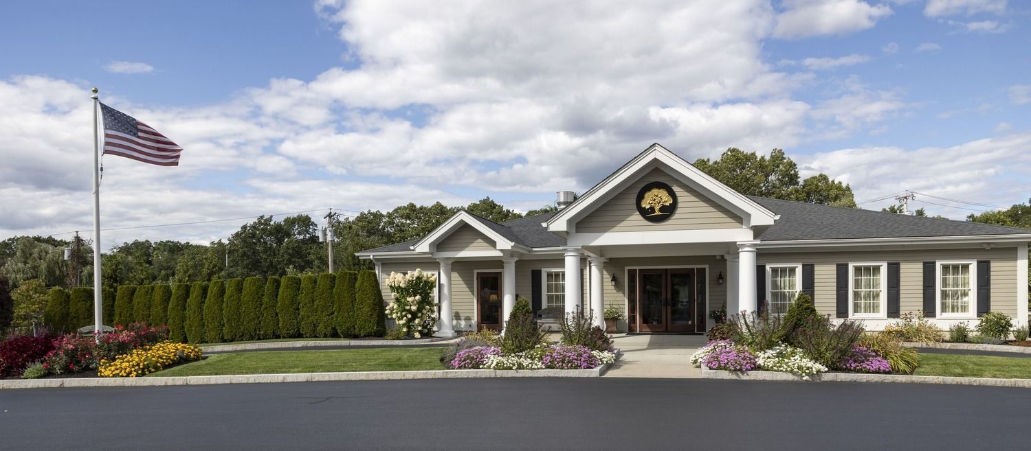 Single-story white clubhouse with American flag, flower beds, and manicured landscaping under a blue sky