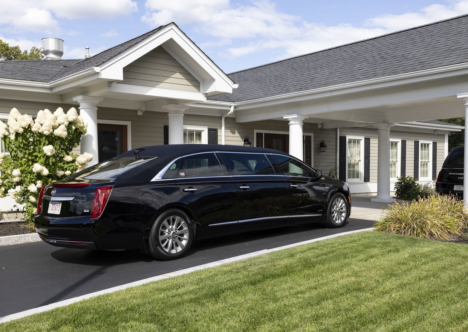 Black luxury sedan parked in front of a white house with a manicured lawn