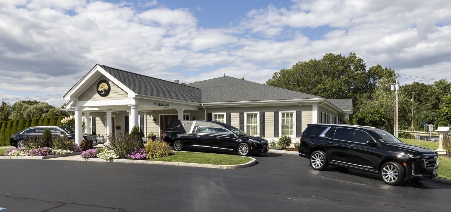 Single-story beige house with black cars parked in front and purple flowers along the driveway
