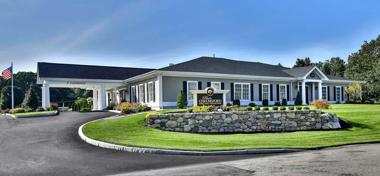 Modern single-story house with a curved driveway, landscaped front yard, and stone garden wall