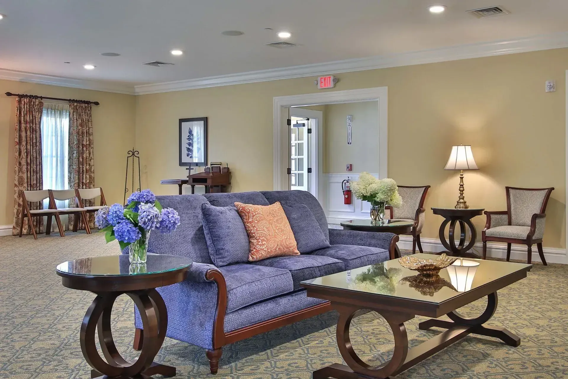 Elegant hotel lounge with blue sofa, floral arrangements, coffee tables, lamps, and chairs