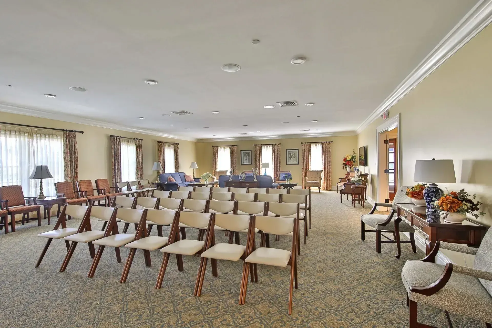 Empty conference room with rows of beige chairs, tables along the walls, and carpeted floor
