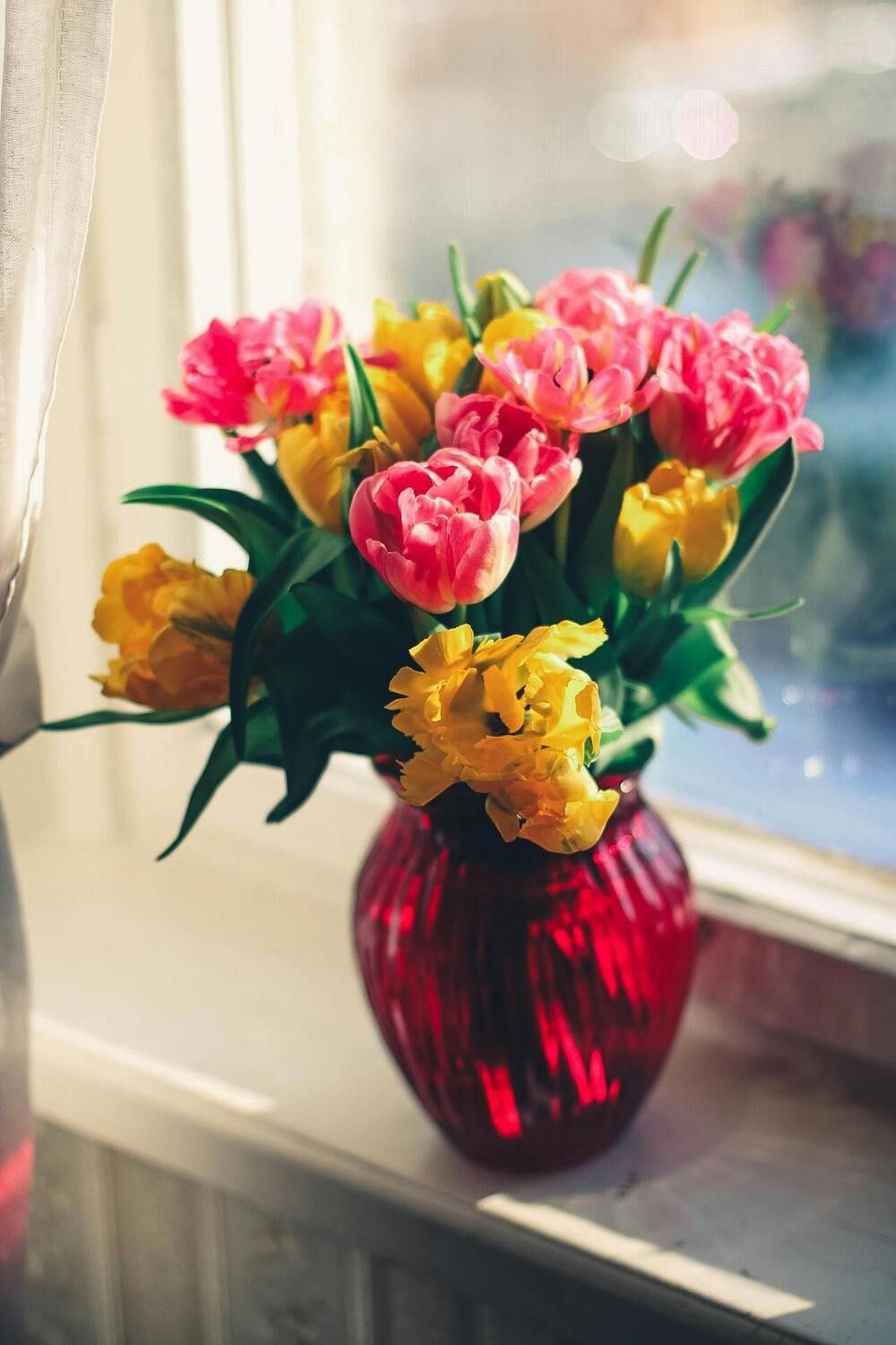 Pink and yellow flowers in a red vase on a windowsill