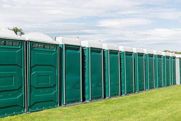 Row of green portable toilets lined up on grass at outdoor event.