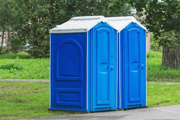 Three blue portable toilets are sitting next to each other in a park.