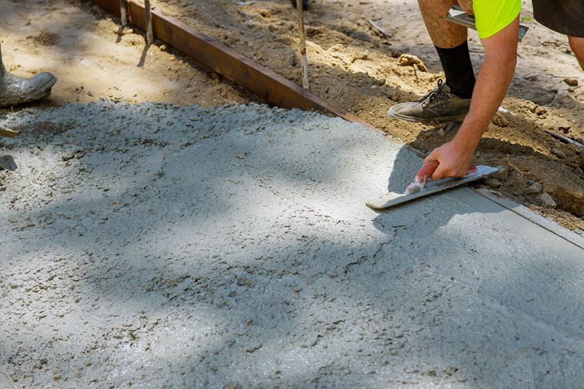 A Man is Using a Trowel to Spread Concrete on a Sidewalk — HMJ Landscapes in Mudgeeraba, QLD