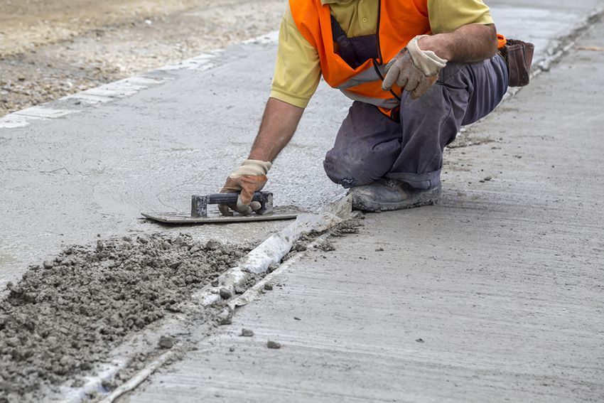 A Man is Kneeling Down and Using a Trowel to Spread Concrete on a Sidewalk — HMJ Landscapes in Burleigh Heads, QLD