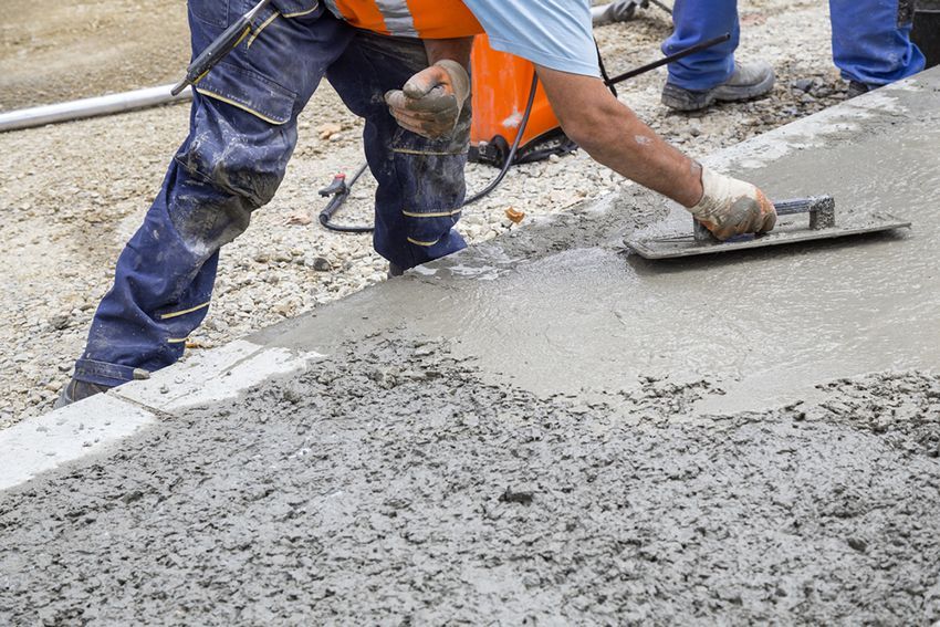 A Construction Worker is Spreading Concrete on the Ground with a Trowel — HMJ Landscapes in Tweed Heads, NSW