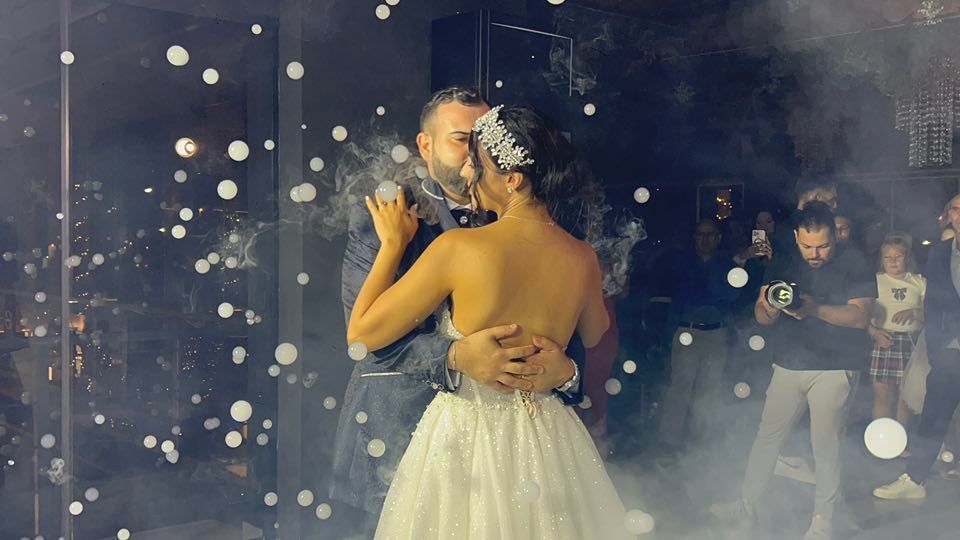 Coppia che balla al ricevimento di nozze con effetti di nebbia e bolle.