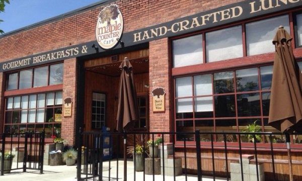 Brick restaurant storefront with large windows, patio umbrellas, and sign reading “Hand-Crafted Lunch.”