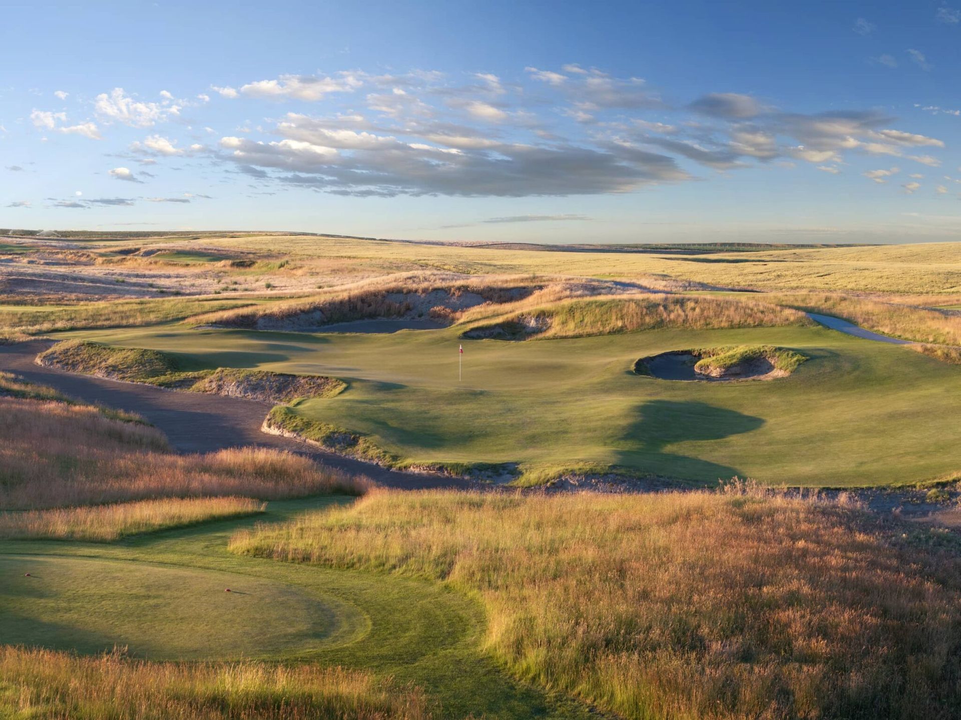 Grassy coastal dunes under a blue sky with scattered clouds, viewed from a high overlook