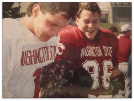 Two Washington State football players smiling beside a black dog outdoors