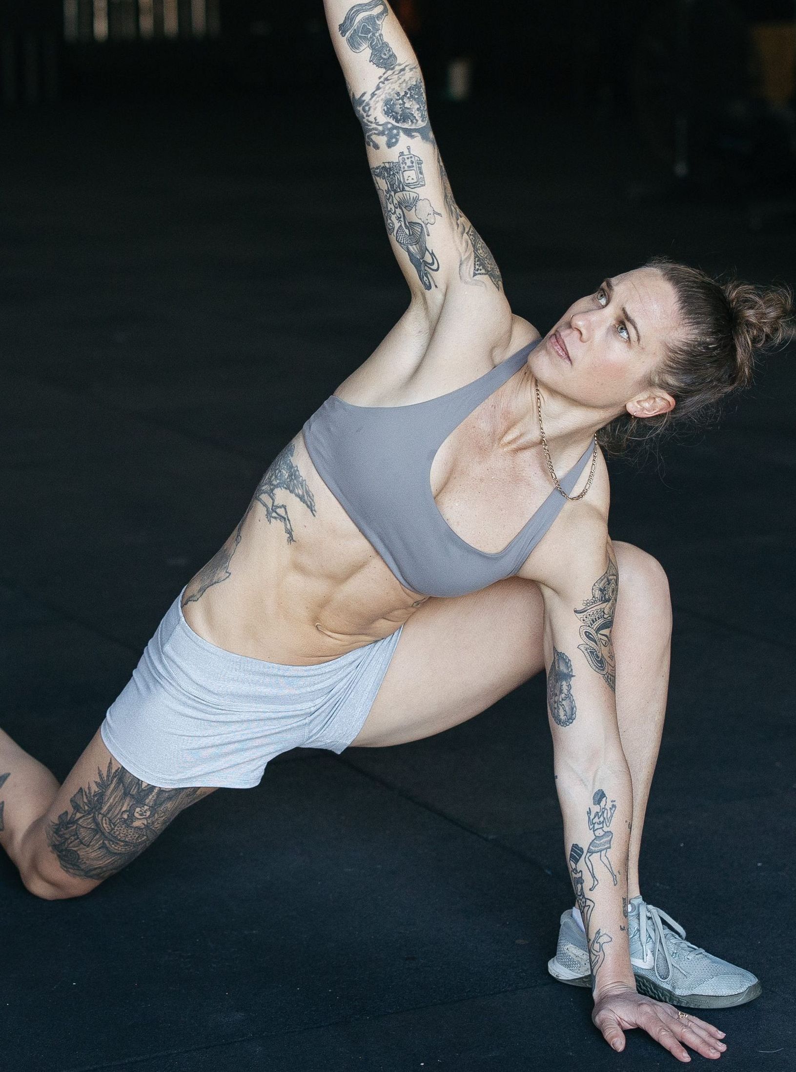 A woman with tattoos is doing a yoga pose on the floor.