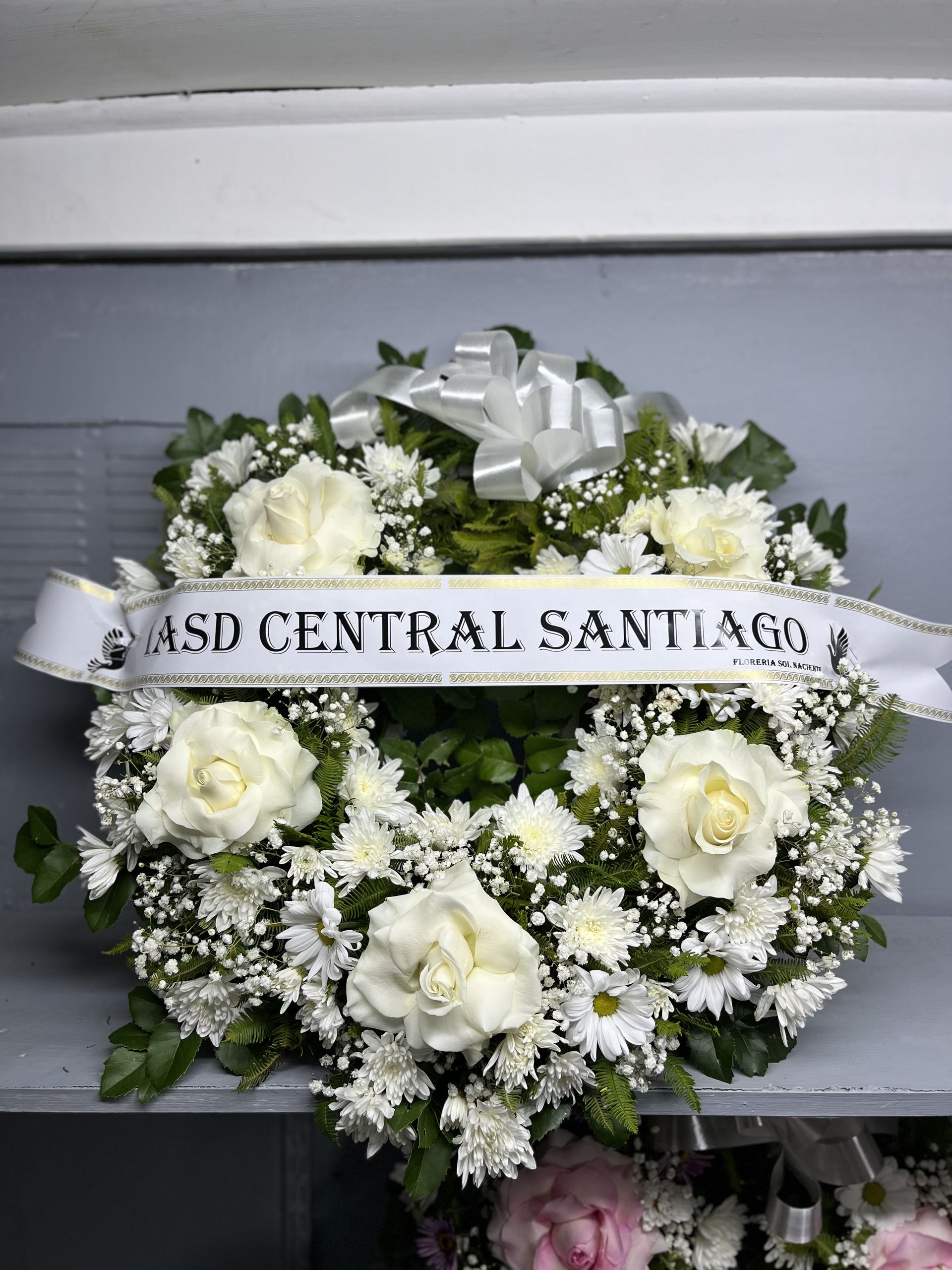 Corona funeraria floral blanca con cinta que dice “4SD Central Satyagraha”