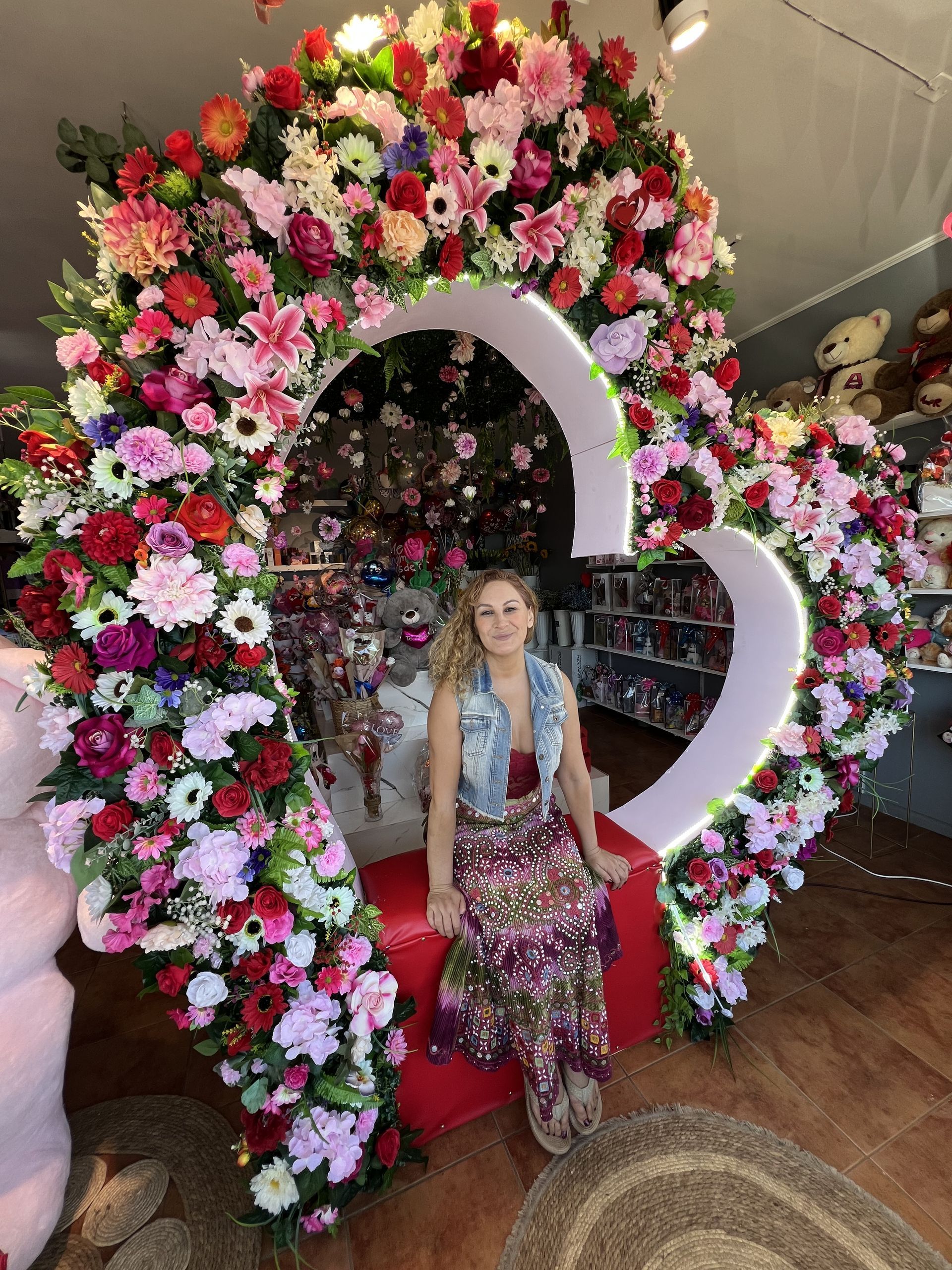 Mujer posando frente a un gran arreglo floral en forma de corazón con flores rosas, rojas y blancas.