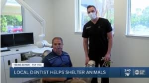 Doctor Andrew Vallo is standing next to a man in a dental chair while holding a dog.