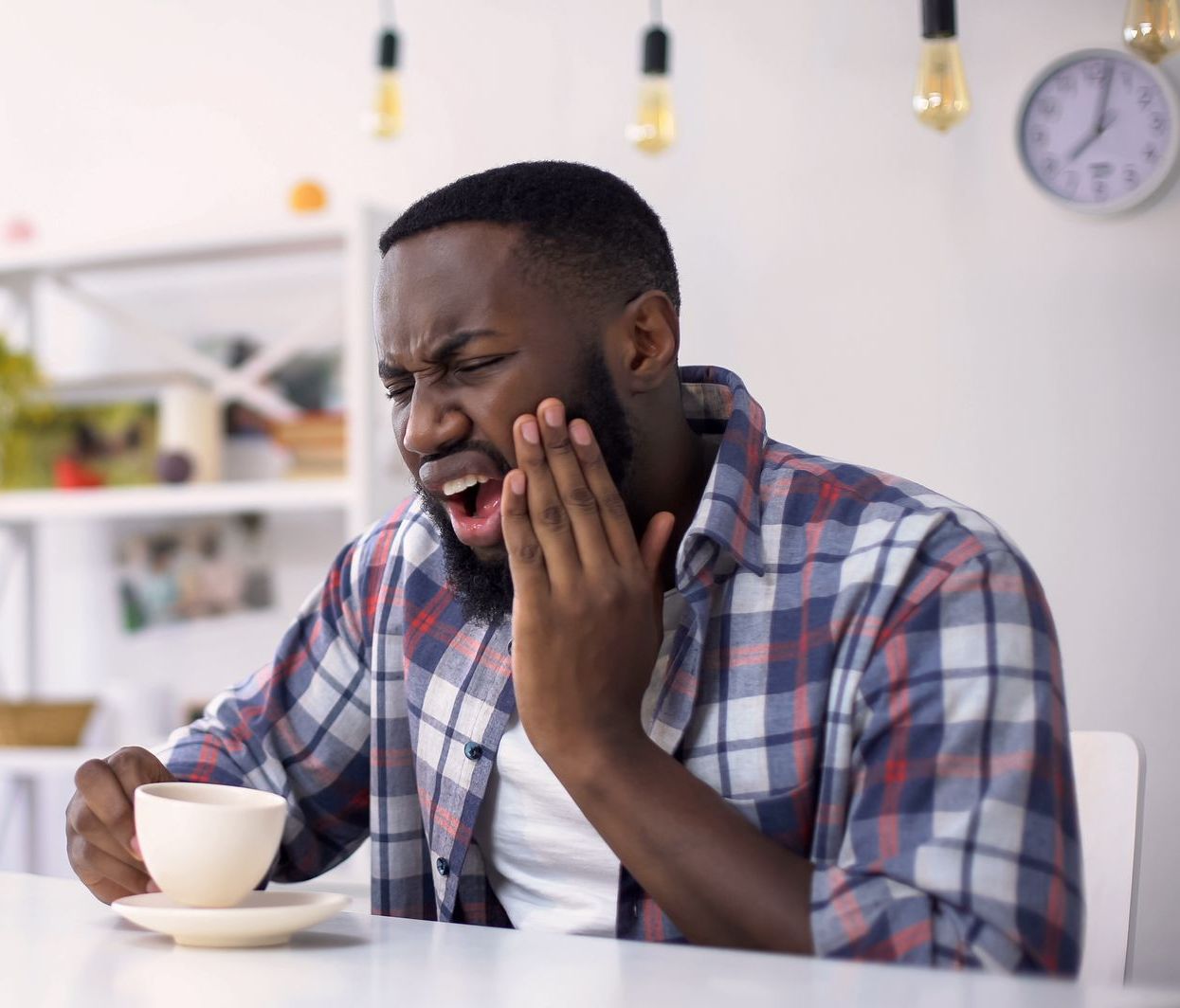 A man is sitting at a table with a cup of coffee and a toothache.