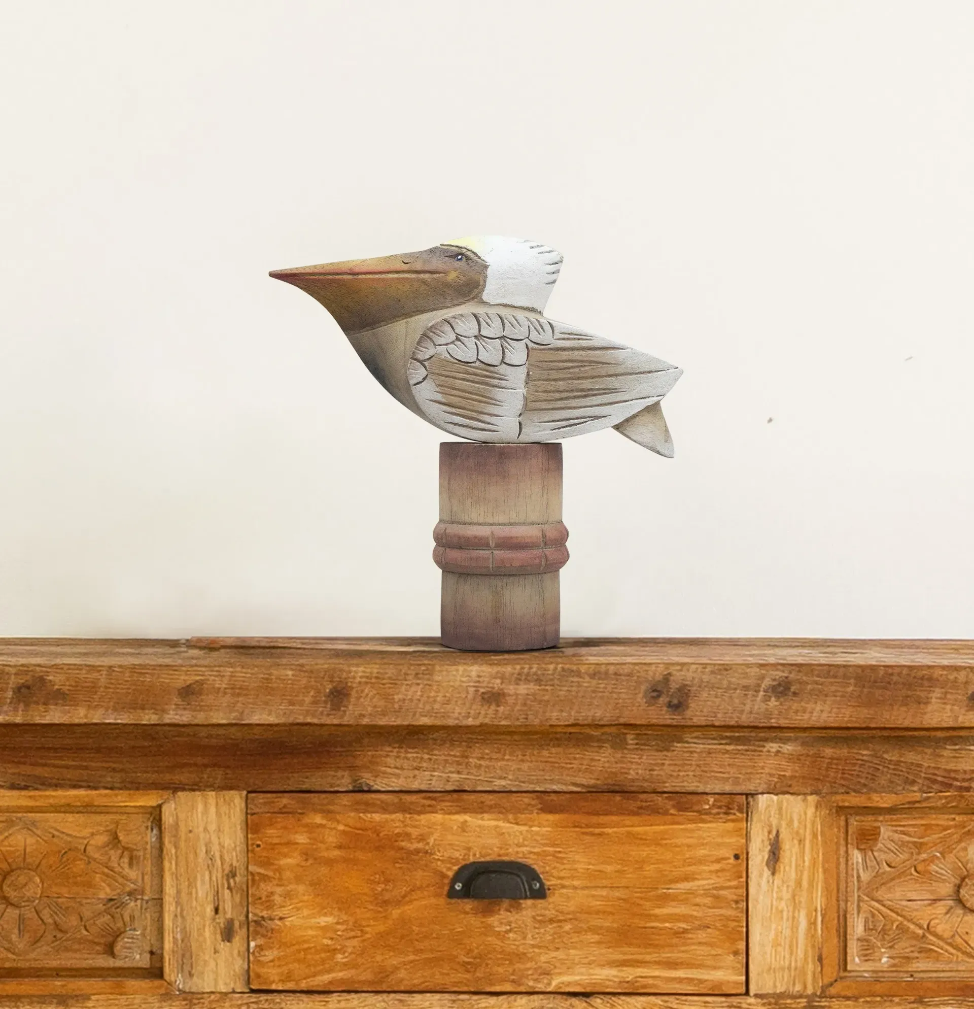 Carved wooden Pelican figurine with a long beak, white head, and tan body on a small pedestal
