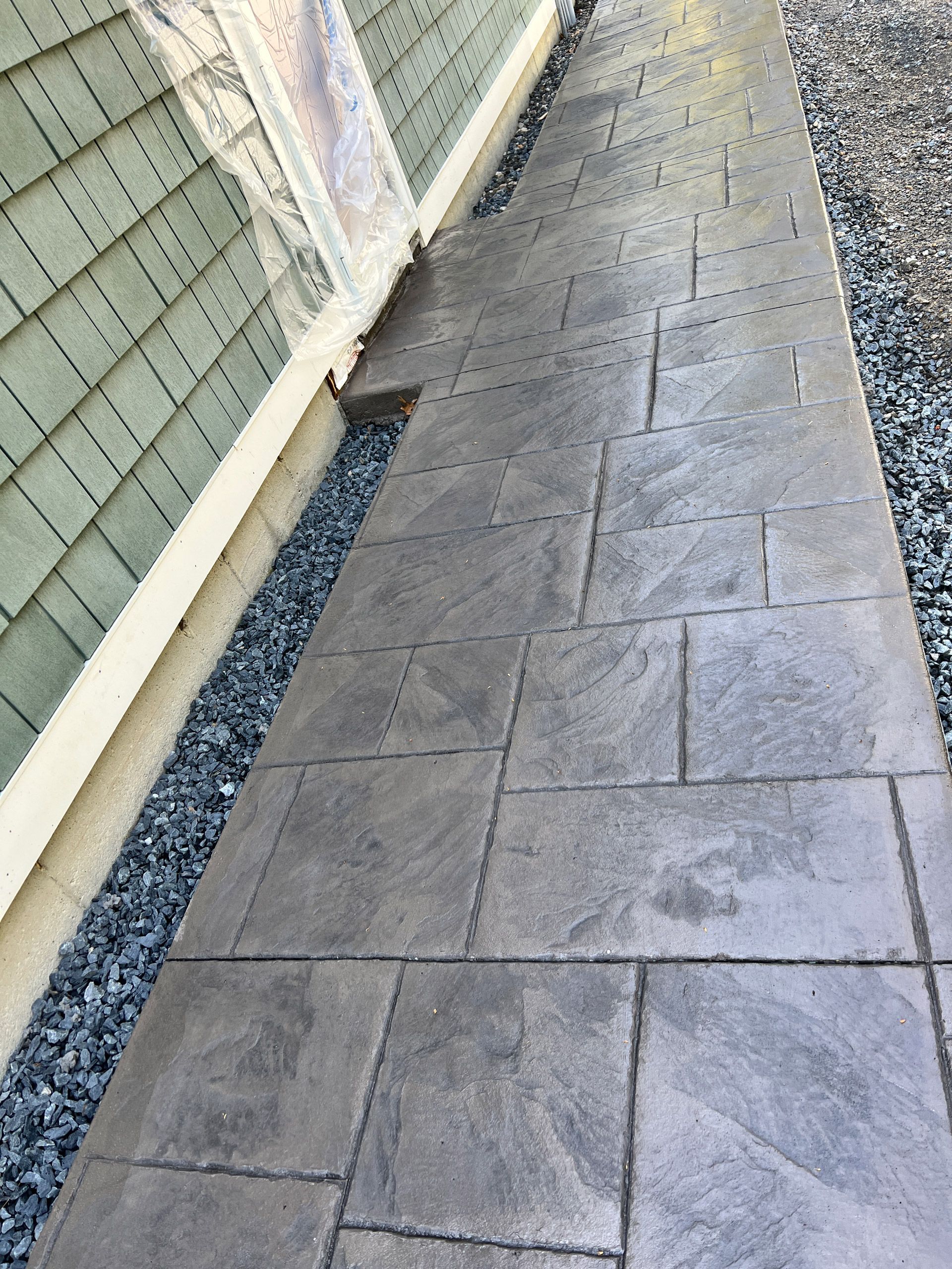 Gray tiled sidewalk beside a building wall with a strip of black gravel along the edge