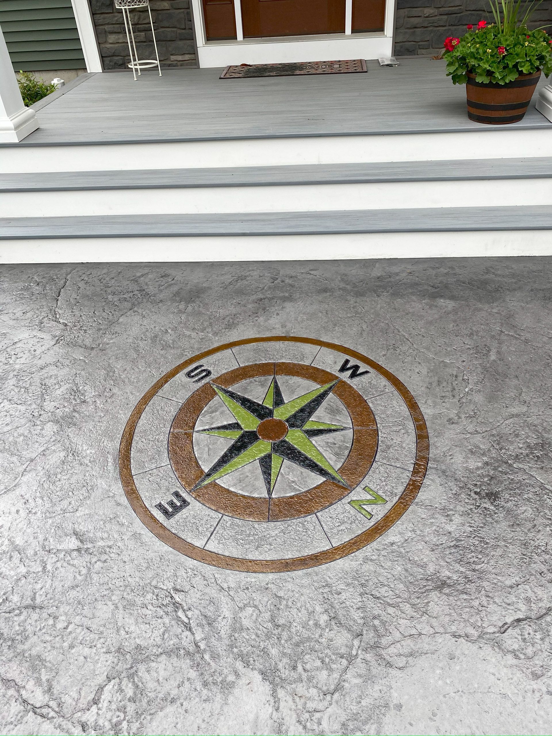 Stone patio with a decorative compass rose inlaid in the center, in front of porch steps and potted flowers