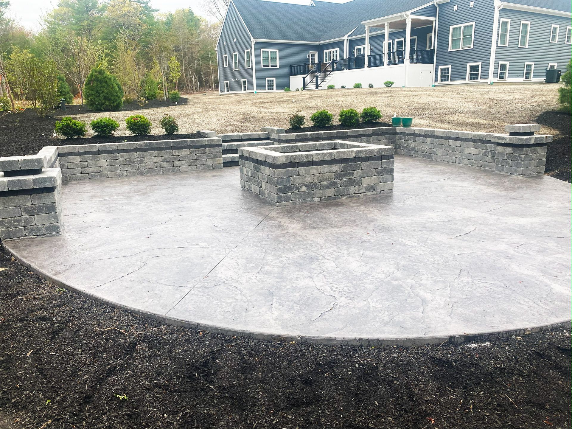 Circular concrete patio with built-in stone benches and a central fire pit in a backyard near a house
