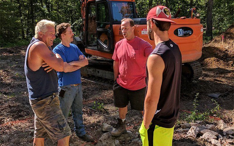 Four people talking beside an orange excavator on a dirt worksite