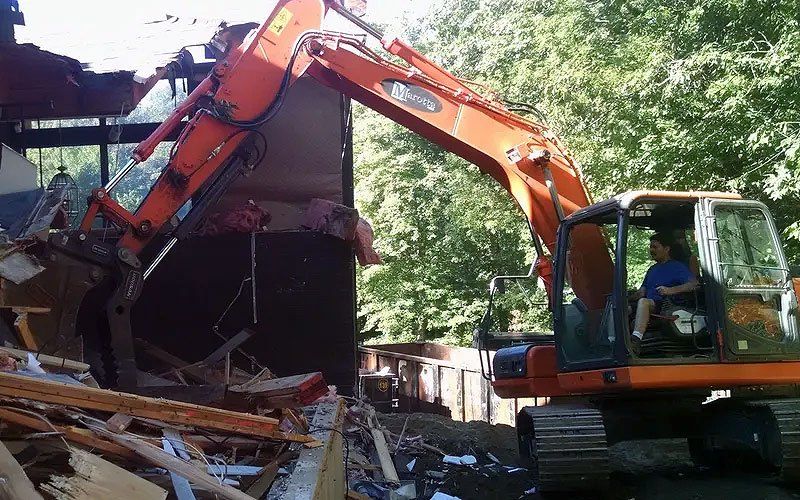 Orange excavator demolishing a building, with debris scattered around
