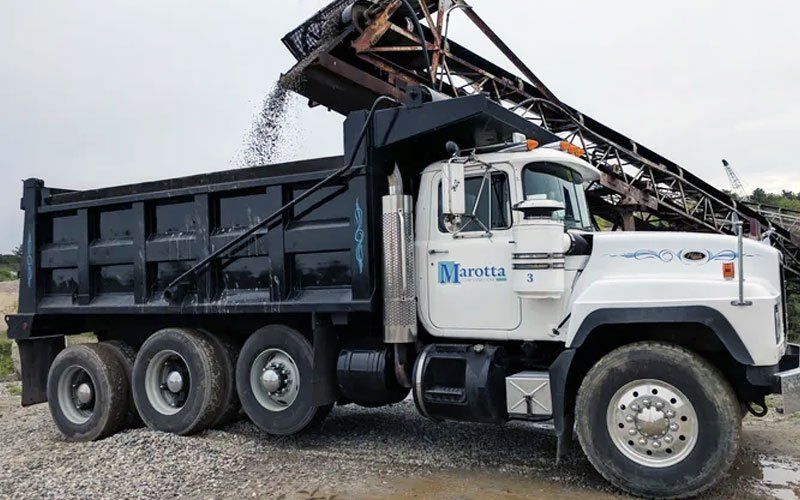 Black dump truck unloading gravel from a conveyor hopper at a construction site