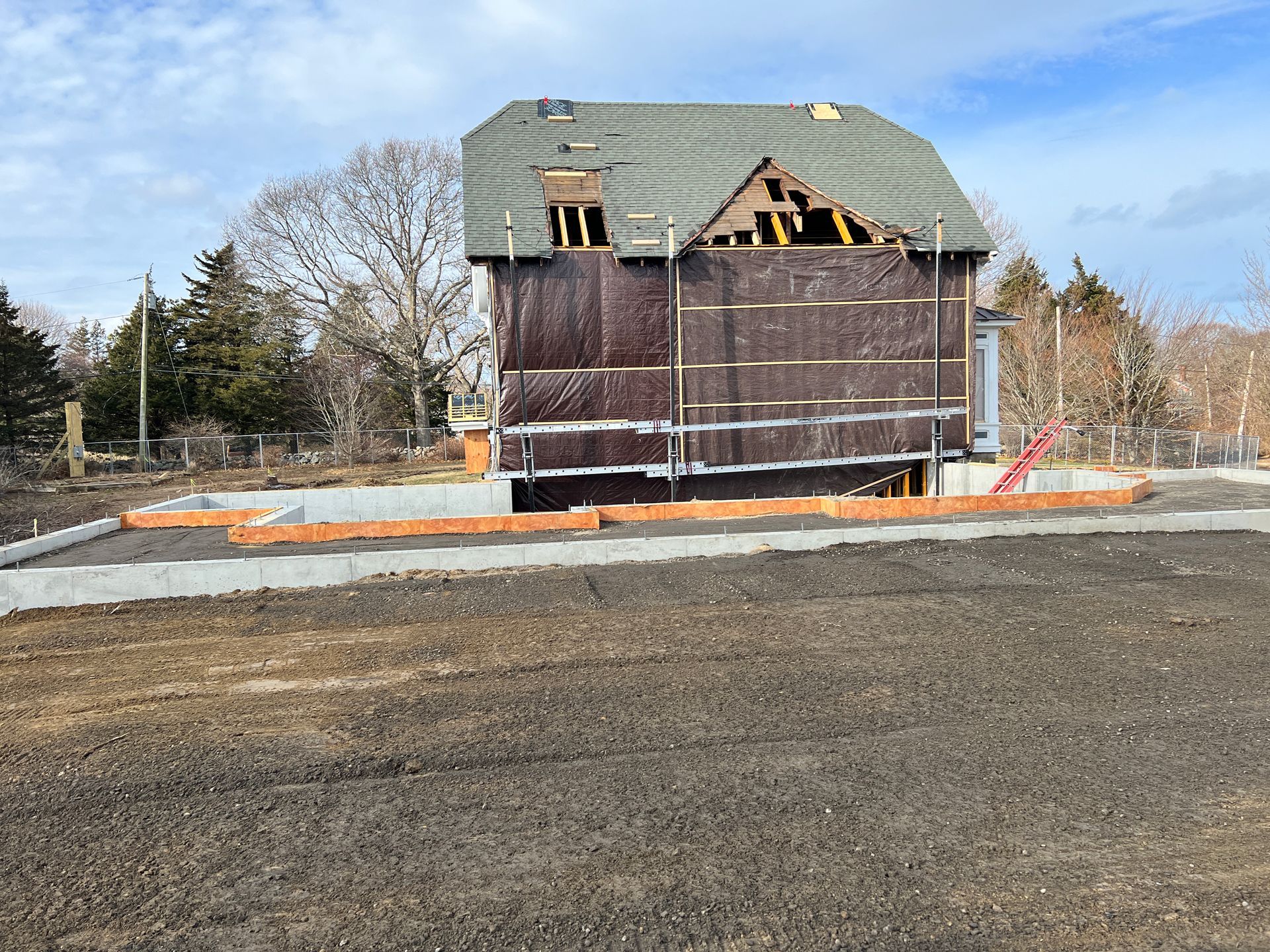 Partially demolished house with exposed roof framing and debris surrounded by a paved lot