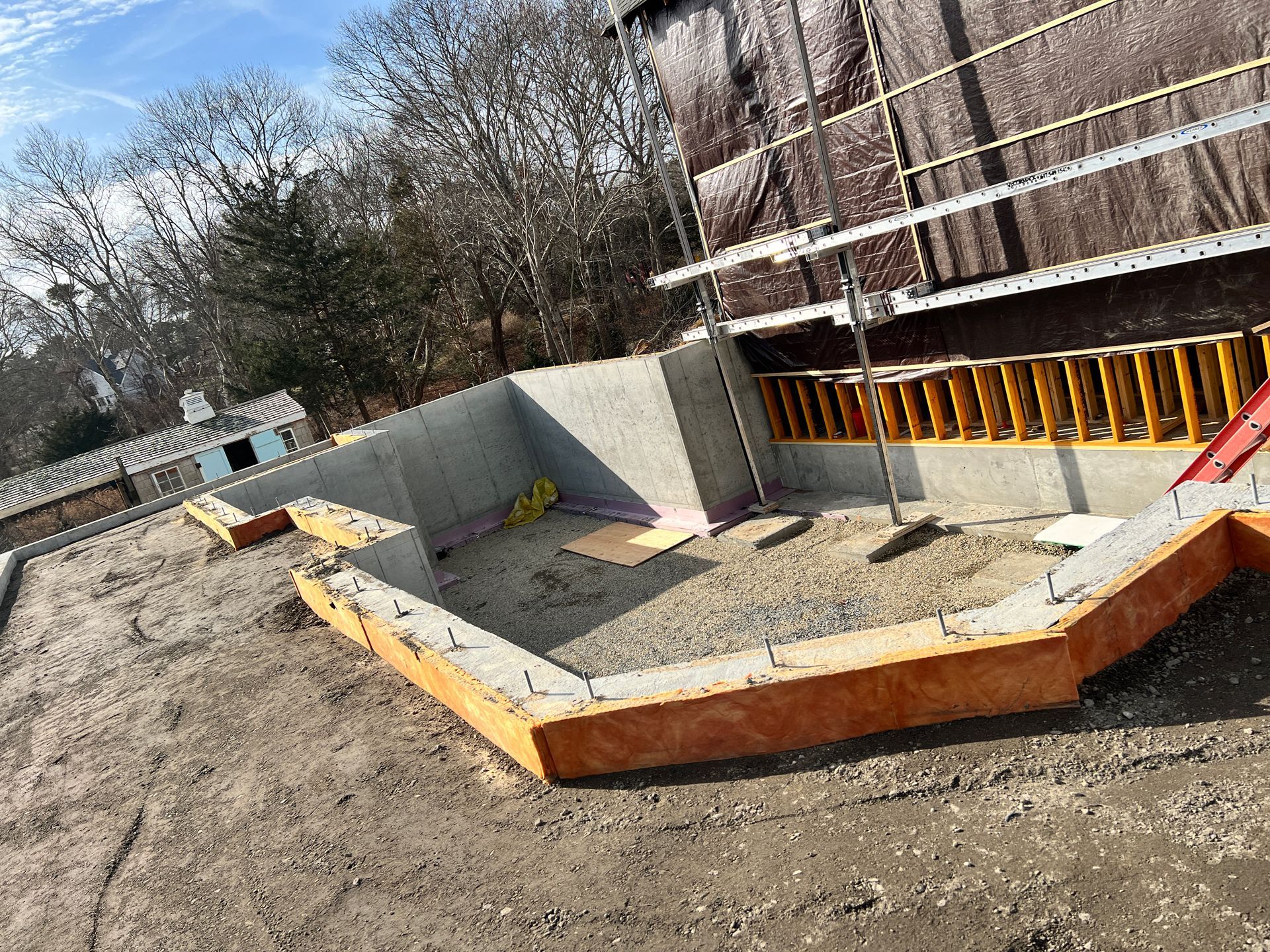 Construction site foundation with concrete walls, orange formwork, and dirt around an unfinished structure