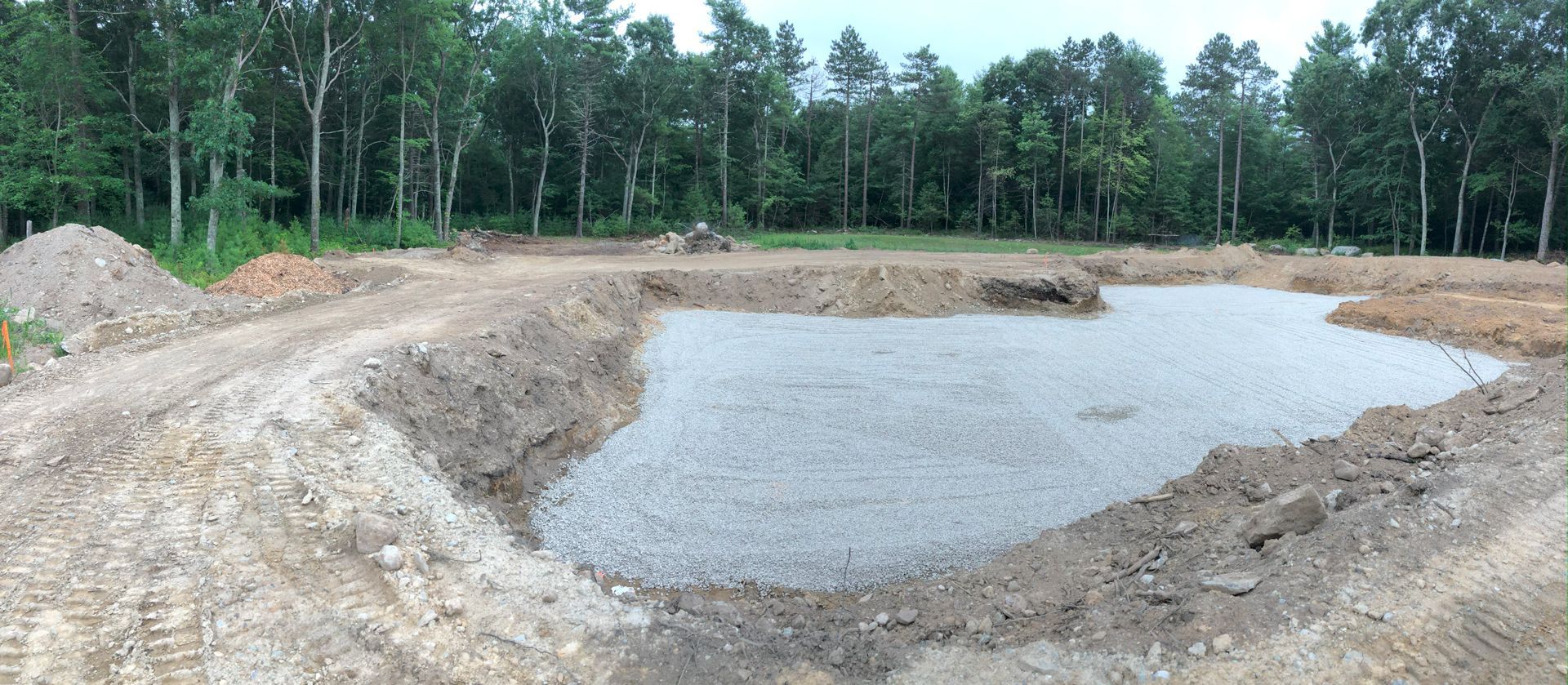 Excavated dirt pit with a shallow water pond beside a forested area