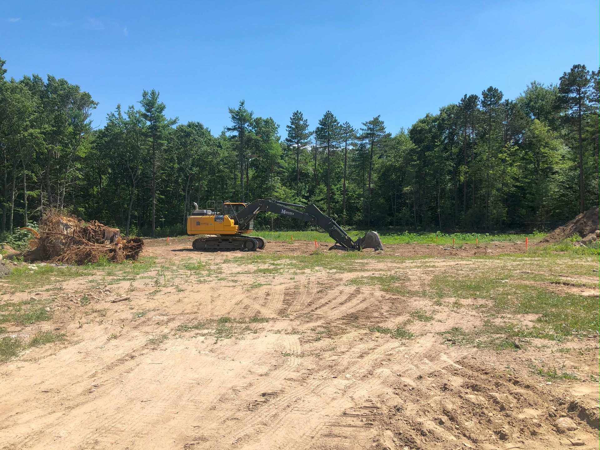 Yellow excavator on a dirt lot with trees in the background under a clear blue sky