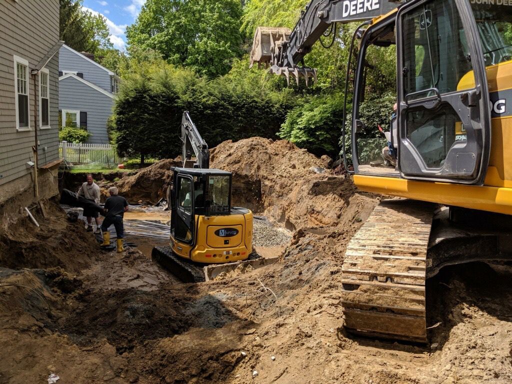 Excavator and skid steer digging a trench beside a house, with a large Deere excavator in the foreground
