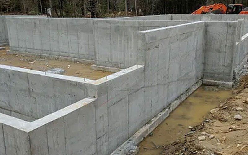 Concrete foundation walls at a construction site with dirt and an excavator in the background
