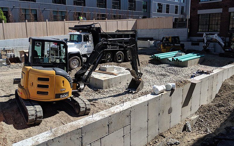 Construction site with excavator beside concrete retaining wall and piles of dirt and debris