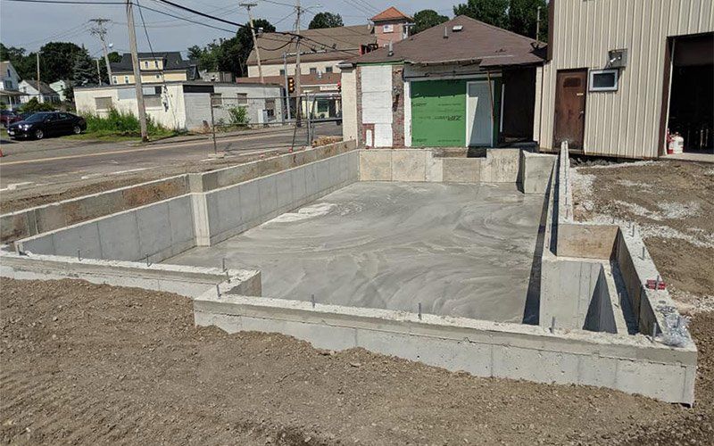 Fresh concrete foundation and retaining walls at a construction site beside houses and garages