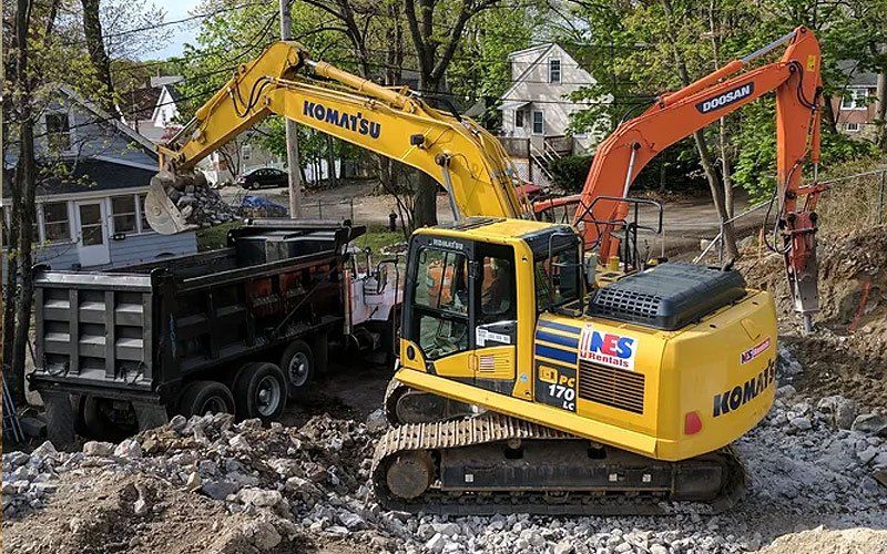 Yellow and orange excavators unloading rubble into a black dump truck at a construction site